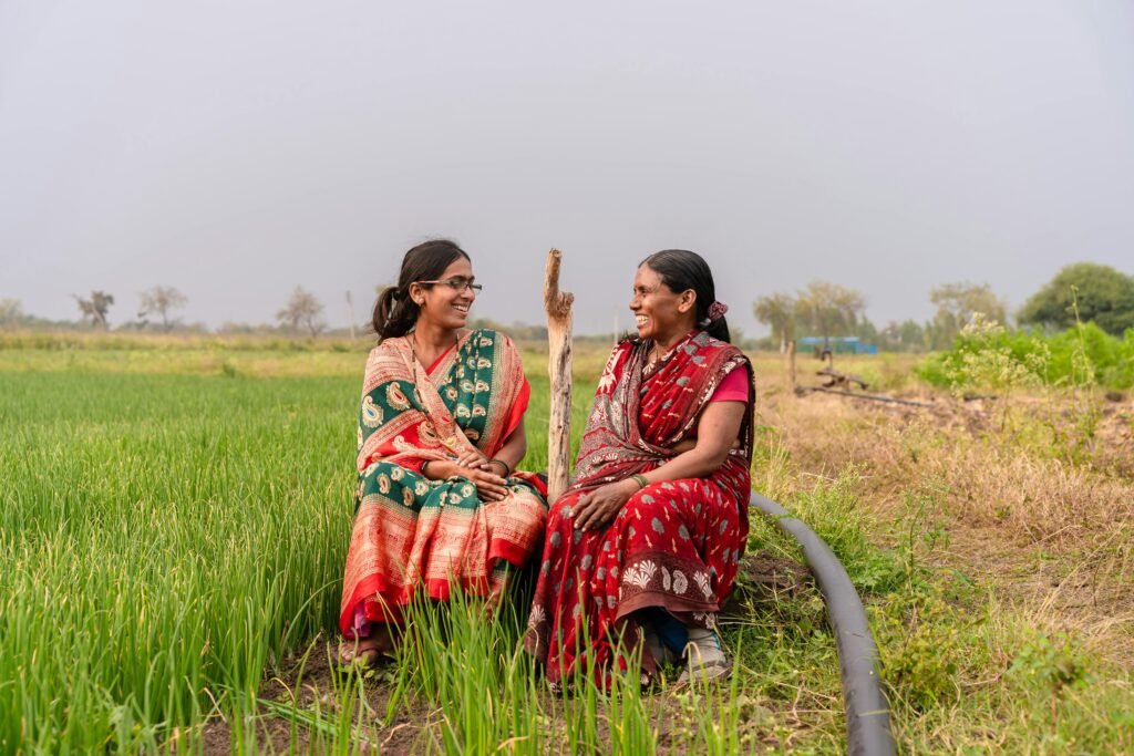 Two women in colorful sarees smiling in a lush green farm in rural Nagpur, India.